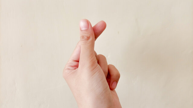 A woman's hand is making a heart hands or love hands gesture, with her index finger and thumb touching, against a plain background. Sometimes it's an expression of affection to loved ones.
