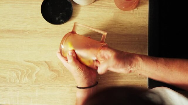 Person holds a clear container with a yellow sponge. The sponge is being pressed down by hands