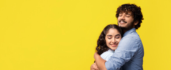 Fototapeta premium A couple stands together in a studio with a bright yellow background. They are embracing each other with smiles on their faces. The scene shows love and connection between them.