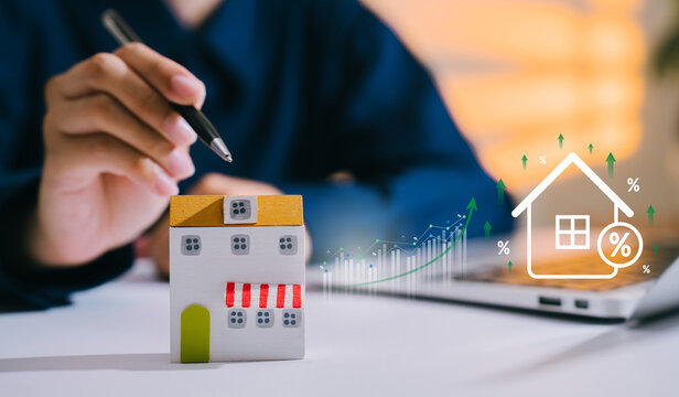 Mortgage rate concept, hand with pen near house model and rising percentage graph, home financing, property investment, loan planning, interest increase, real estate market outlook
