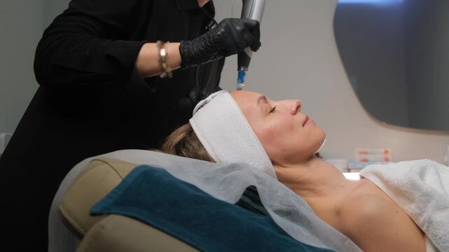 Cosmetologist performing a rejuvenating microneedling therapy on a woman's face in a clinic