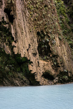 turquoise  lake and wet limestone cliff covered with moss, and fern and other hanging plants, Tumalog Falls, Cebu, the Philippines
