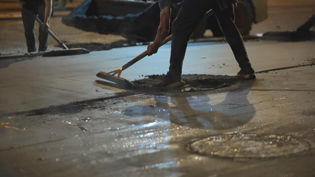 Night shift workers spreading hot asphalt for new road construction