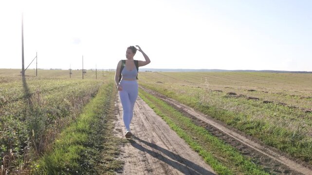 A woman with a backpack in sportswear walks through a field on a bright sunny day on a hike