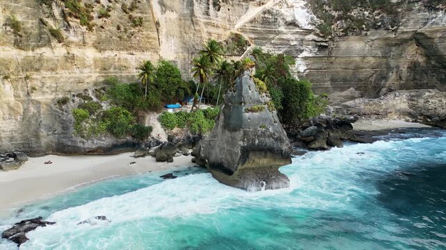 Aerial drone view of the iconic limestone rock formation at Diamond Beach, Nusa Penida, Bali, Indonesia. Turquoise waves crash against the massive sea stack surrounded by towering white cliffs and tro