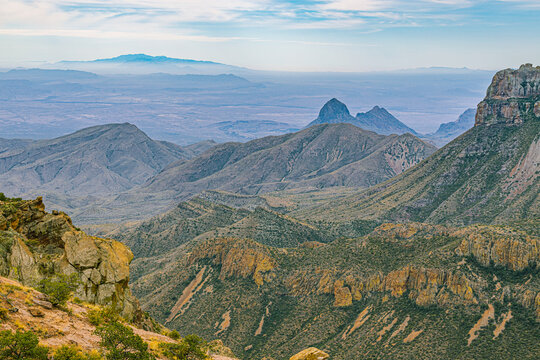Broad panorama of rugged peaks and ridges with distant desert plains under a partly cloudy blue sky.