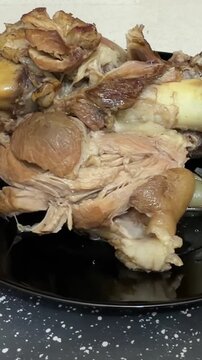 Close-up of cooked pork knuckle on black plate, vertical food video showing tender meat, bone and rich gelatin texture of traditional pork shank ready to serve for dinner