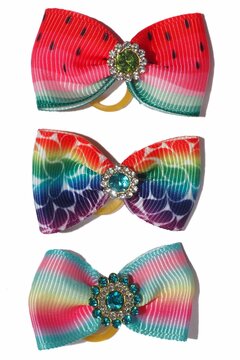 Set of vibrant pet grooming bows with elastic bands and decorative gems. Bright summer-inspired designs including rainbow, fruit, and candy patterns on white background.
