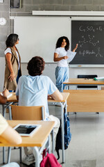 Young female student presenting academic lesson in classroom. Diverse people participating in a high school learning activity together. Education and presentation concept.
