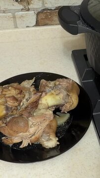 Close-up of cooked pork knuckle on black plate in home kitchen, vertical food video showing traditional boiled pork shank with bone, tender meat and gelatin skin ready to serve