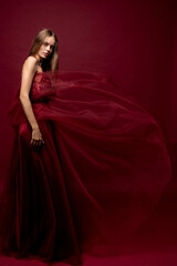 Fototapeta premium Fashion model poses in flowing red dress against a deep red background in an artistic studio setting