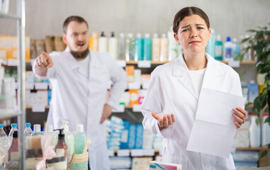 Confused female pharmacist employee during argument with boss. Subordinate with documents in hands,...