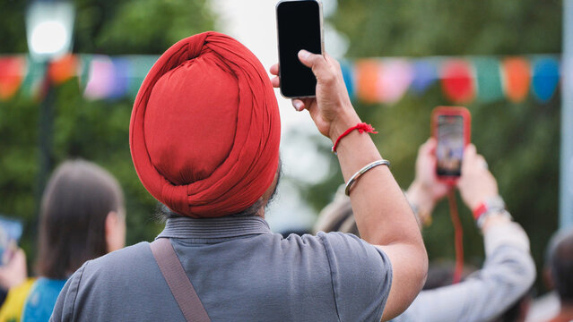 Sikh man in red turban filming celebration with smartphone at India Day in Moscow