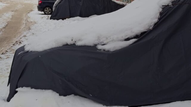 Row of vehicles covered in icy snow. Lineup of covered cars resting in snow beside icy curb under muted urban cold atmosphere