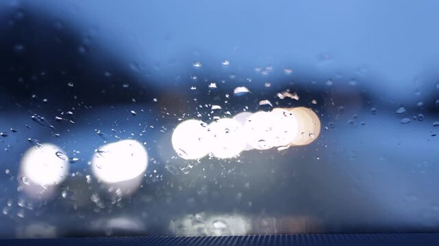 Raindrops on windshield with blurred oncoming car headlights. Rainy cinematic bokeh background.