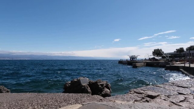 Waves crashing softly on the Adriatic Sea coastline in Lovran, Croatia. Real time blue water splashing on the beach on a windy sunny spring day. Continuous motion of the sea surface with copy space.