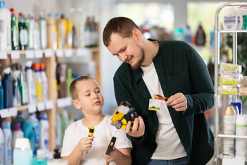 Family schoolboy son and dad are choosing hand tools in store. Customer reads label, compare...