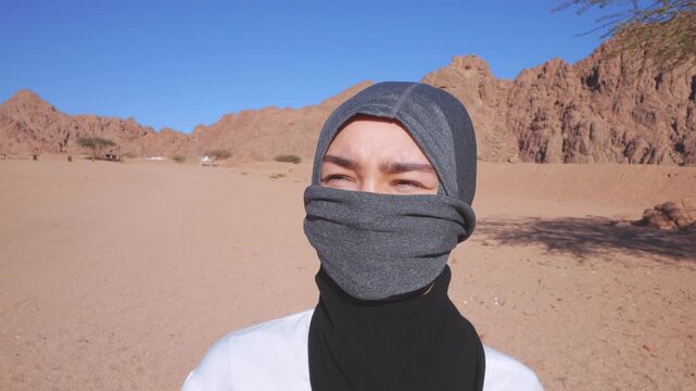 Close-up of a young Bedouin girl wearing a traditional gray niqab face veil and headscarf in the rocky desert.