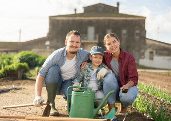 Fototapeta premium Family of farmers with a watering can and a hoe in the garden after planting seeds. Farmers grow organic and organic vegetables. Portrait of a family on a farm