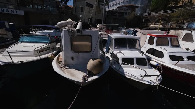 White small fairytale fishing boats rocking in the harbour of Lovran, Croatia. Real time side view of an Adriatic Sea port. Sunny spring day in the Kvarner Bay. Everyday life in a travel destination.