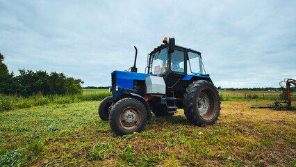 Blue tractor parking in harvested field after mowing grass
