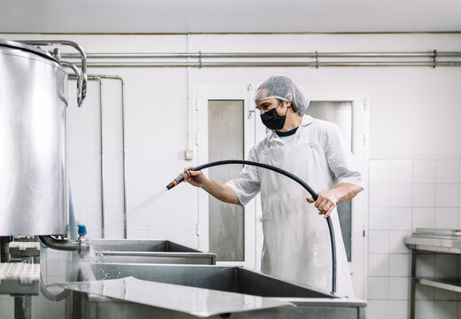 Worker cleaning dairy factory equipment with water hose