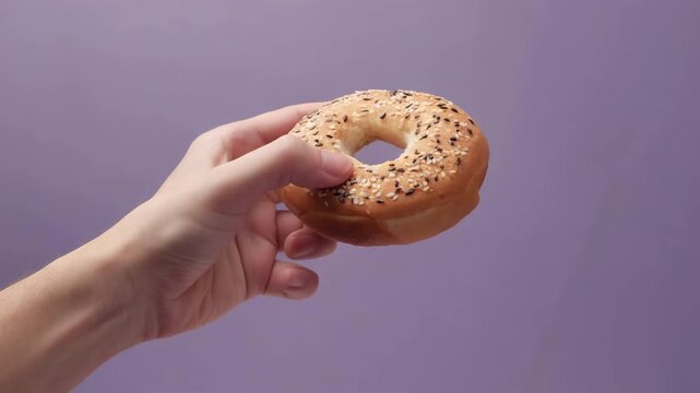 ラベンダーの背景でベーグルを指に通して持つ手