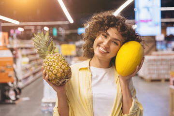 Happy woman holding pineapple and melon fruit, shopping for healthy food in a grocery supermarket