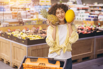 Happy woman experiencing fresh fruit choosing pineapple and melon in a supermarket grocery store