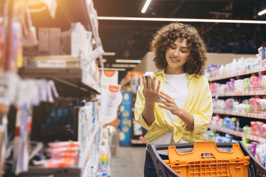 Smiling woman shopping at grocery store, comparing product labels and making purchasing decision