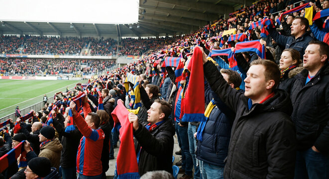 Passionate football supporters cheering in a crowded stadium stands while holding up team scarves during an intense match as a symbol of sports fandom loyalty and the exciting atmosphere of a live gam