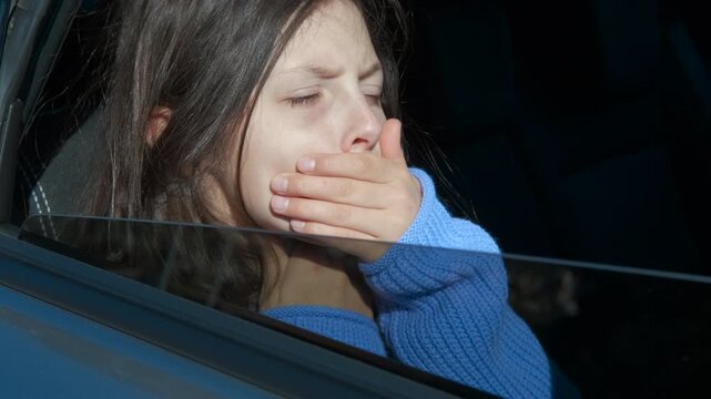 Young girl feeling nauseous and sick during car trip. Profile view of a young girl with long brown hair sitting in a car and feeling unwell, experiencing motion sickness as she touches her face