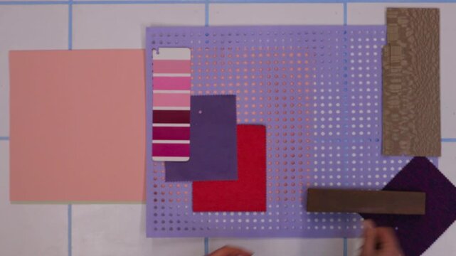 Top view of designer arranging colorful materials, fruit slices, flowers and texture samples to create moodboard and color palette for design project. Flat lay creative process with hands, visual comp