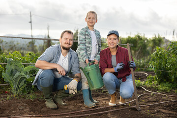 Fototapeta premium Family of farmers with a son in the garden after planting seeds. Generation of farmers grows quality products. Farmers plant seeds in cultivated land
