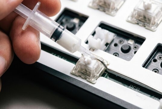 Modder applying white lubricant to a mechanical keyboard switch stem using a syringe