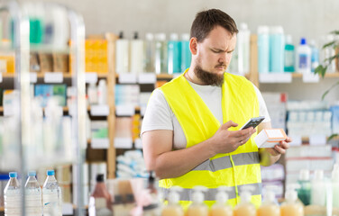Young man builder in uniform scanning qr code for box of pills in pharmacy