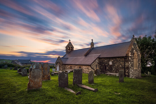 Long exposure of historic St Gwyndaf stone church with graveyard at sunset, featuring weathered gravestones and lush green grass in Llanwnda, Pembrokeshire, Wales