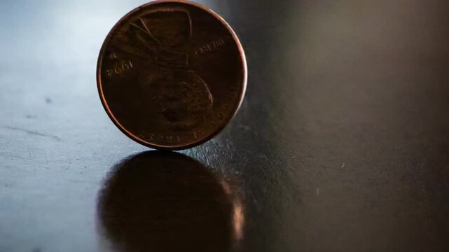 Slow motion close up of a penny spinning on a wooden table until it lands on heads