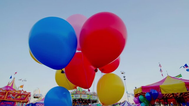 Many colorful balloons floating above a funfair carousel. Festive amusement park background with tents and rides