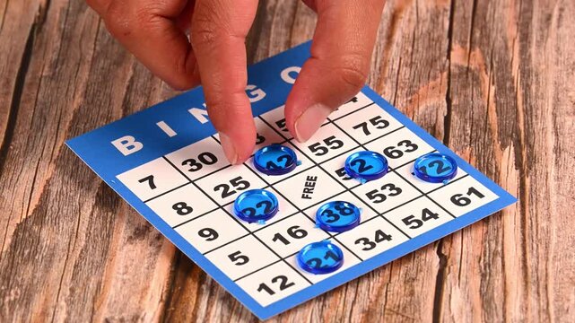 Close-up of person playing bingo with blue markers on a wooden table
