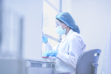 Fototapeta premium Professional surgeon working in sterile biosafety cabinet carefully. Female doctor preparing for operation in hospital laboratory. Female worker checking manufacturing standard in clean factory lab.