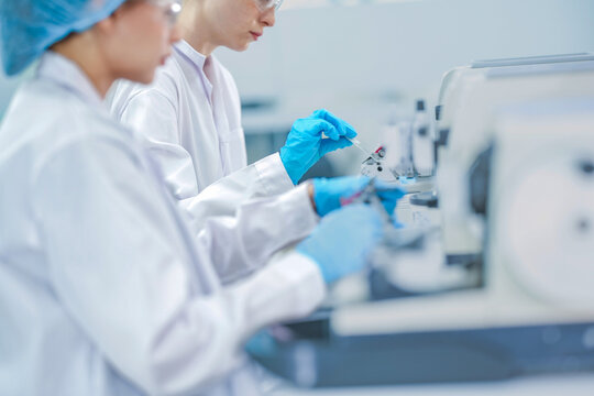 histology technician cutting tissue section with rotary microtome. Female scientist processing paraffin biopsy block in lab. Doctor in protective gear using microtome machine to analyze tissue sample.