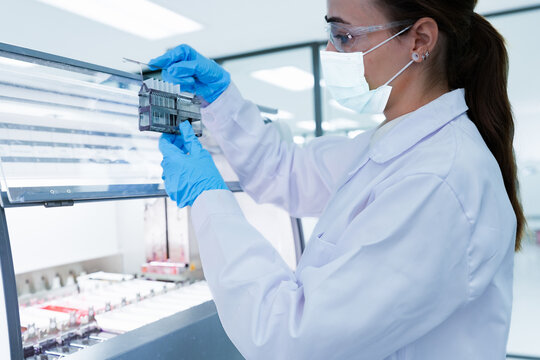 Medical scientist loading slide rack into automated stainer machine. Lab technician in protective gear processing histology samples in sterile hospital laboratory.