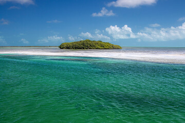 Fototapeta premium A small tropical island surrounded by green water and blue sky with clouds