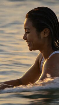 Happy asian surfer girl paddling on surfboard at sunset