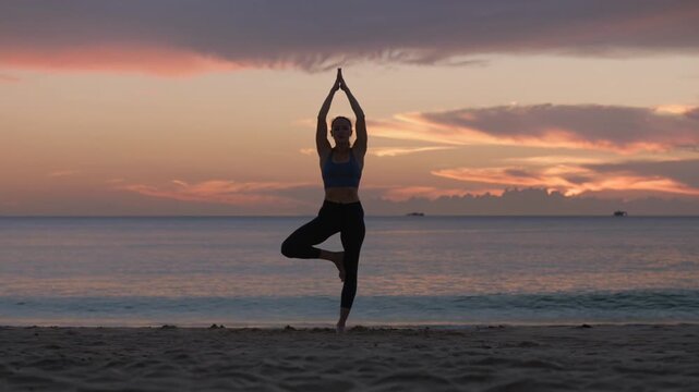 Silhouette of a woman practicing yoga tree pose on the beach at sunset