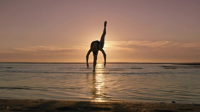 Silhouette of a flexible gymnast performing acrobatic handstand at sunset