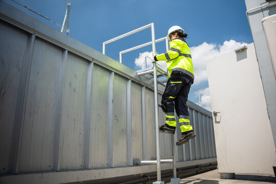 Professional maintenance worker in hard hat and safety gear ascending to inspect HVAC systems, Woman engineer climbing a metal ladder for technical installation at construction site