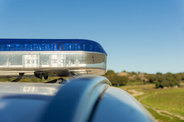 Public safety concept: Close-up of blue emergency police light bar on patrol car with rural landscape background. © Ivanb