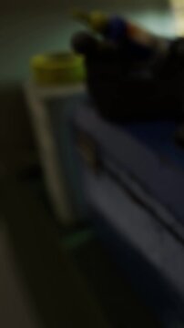 A table is cluttered with various items in a room. Different objects are scattered across the surface. Light enters through a window.